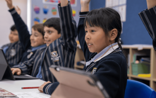 A photo of several St Vincent's College Ashfield enthusiastically raising their hands in a classroom on the journey to 2025 NAPLAN success